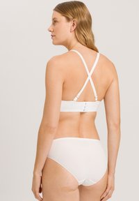 Bílá podprsenka a bikiny s kříženými pásky. Jednoduchý design, hladká textura a nastavitelné kovové detaily. Světlá barva bez vzorů.
