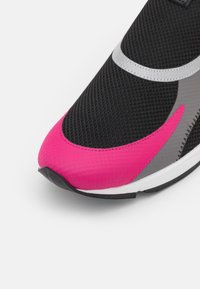 Černé síťované tenisky s růžovým špičkovým krytem, šedými akcenty a texturovaným černým tělem s bílou podrážkou. Vyznačují se kontrastními barevnými detaily.