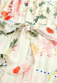 Tessuto leggero con motivo floreale che presenta fiori rosa, rossi e gialli su uno sfondo crema, con vita legata e texture morbida.