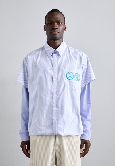 Kurzärmliges, hellblau gestreiftes Button-Up-Hemd mit einem kontrastierenden Langarmunterhemd, das zwei Friedenstauben-Patches auf der Tasche zeigt.