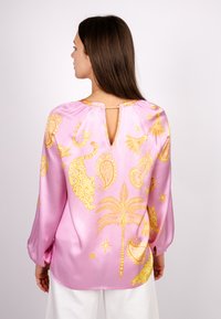 Rosa Satinbluse mit gelb bedrucktem Paisley, Leoparden und Palmen; lange Ärmel mit Knopfmanschetten und einer Schlitzöffnung am Rücken.