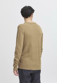 Lys brun strikket genser med rund hals, lange ermer og teksturfinish. Litt lengre bakstykke, minimalistisk design.