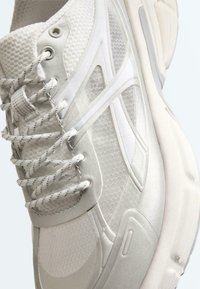 Gros plan sur une basket de sport blanche présentant un tissu en mesh texturé, des lacets à motif, et une semelle épaisse et rembourrée.