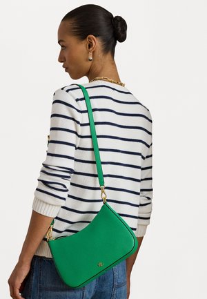 Borsa a tracolla verde in pelle con una forma curva, hardware dorato e un logo sottile. Indossata sopra un maglione a righe bianche e navy.