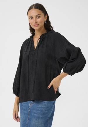 Black, textured blouse with a ruffled neckline, tie closure, and button detail. Features puffed sleeves and a relaxed fit.