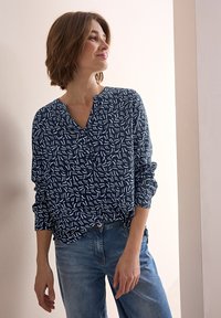 Marinblus med vitt abstrakt mönster, V-ringning, långa ärmar och mjukt tyg, kombinerad med ljusblå denimjeans.