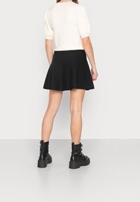 Svart utsvängd kjol kombinerad med en krämfärgad topp med puffärmar; modell som bär svarta plattformsskor med fotled och spännen. Släta texturer.