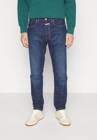 Mörkblå denimjeans med raka ben, med knäppning, subtil sömnad och kombinerade med ljusa sneakers.