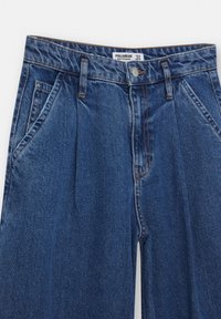 Höga blå denimbyxor med veck, sidofickor och knappstängning av metall. Har kontrasterande orange sömmar.