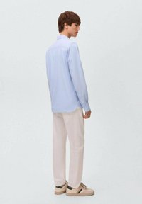 Camicia a maniche lunghe azzurra, vestibilità comoda con orlo curvo, abbinata a pantaloni color crema e sneakers beige con strisce verdi.
