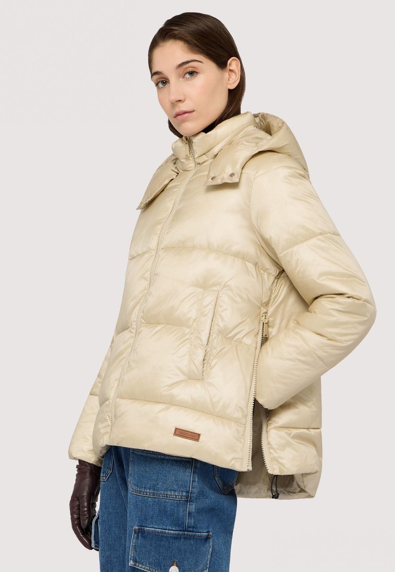 Beige péřová bunda s lesklým povrchem, s kapucí, velkými prošívanými částmi a zipovým uzavřením. Kožený detail poblíž lemu.