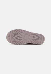 Suela de zapatilla lila con patrón de tracción geométrico, logo circular en el centro y una textura suave para mejorar el agarre.