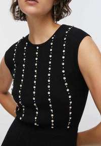 Top nero senza maniche con file verticali di strass rotondi trasparenti su una texture a coste, che crea un design strutturato.