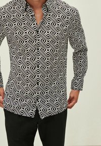 Camisa de manga larga en blanco y negro con un patrón en espiral, que presenta un cuello abotonado y acentos de botones en contraste.
