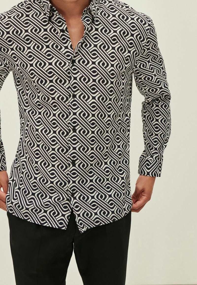 Camisa de manga larga en blanco y negro con un patrón en espiral, que presenta un cuello abotonado y acentos de botones en contraste.