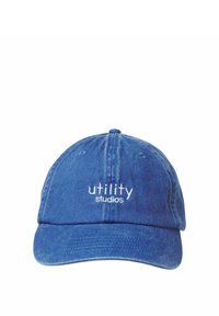 Blå denimkasket med en buet skygge og hvid broderet tekst "utility studios" på fronten. Blød tekstur med syningsdetaljer.