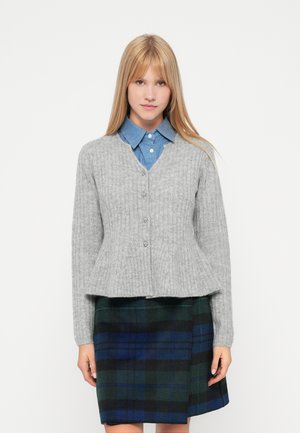 Siva rebrasta kardigan z V-izrezom, sprednjimi gumbi in peplum robom, nošen čez modro srajco s kragnjo in karo krilo v zeleni in mornarsko modri barvi.