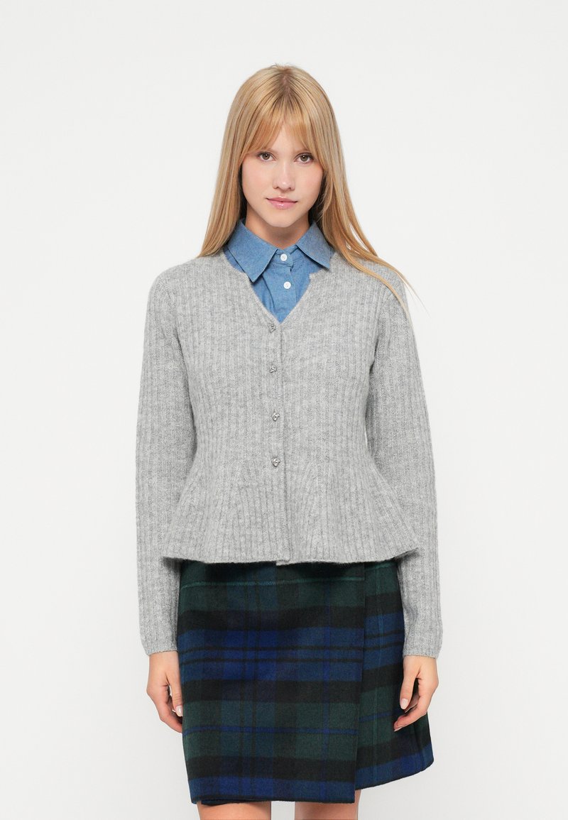 Siva rebrasta kardigan z V-izrezom, sprednjimi gumbi in peplum robom, nošen čez modro srajco s kragnjo in karo krilo v zeleni in mornarsko modri barvi.