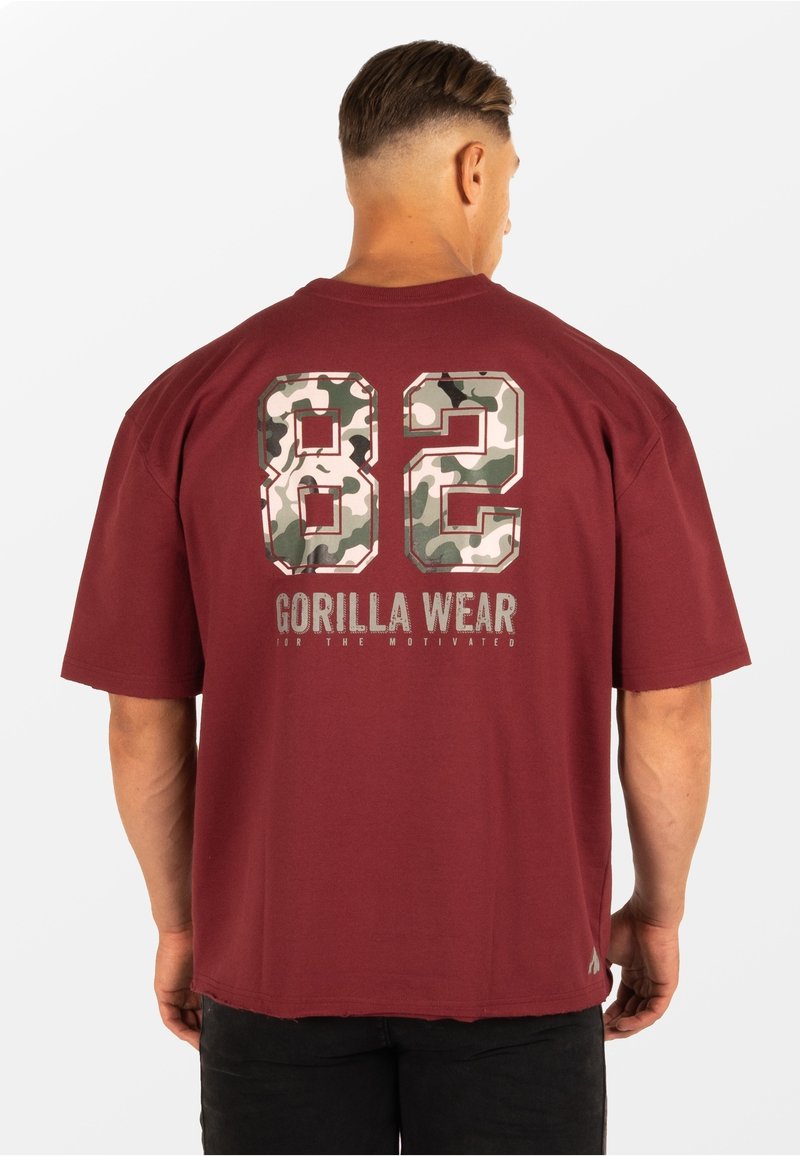 Bordeauxkleurig t-shirt met korte mouwen en grote camouflage cijfers "82" op de achterkant, met daaronder de tekst "GORILLA WEAR". Zacht, casual materiaal.