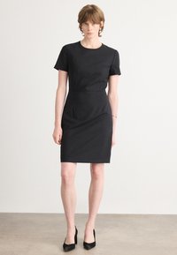 Black short-sleeve dress with a round neck, fitted design, and knee-length hem. Made of smooth fabric, featuring a simple silhouette.