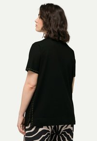 Camiseta negra de manga corta con tachuelas doradas decorativas a lo largo de las costuras laterales; corte holgado; tejido suave; combinada con pantalones con estampado de cebra.