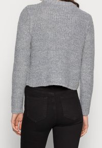 Szary sweter dziany o prążkowanej fakturze, krótki fason, z długimi rękawami i okrągłym dekoltem, zestawiony z czarnymi dopasowanymi dżinsami.