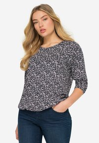 Blusa blu navy a fantasia floreale con maniche a tre quarti, scollatura rotonda e tessuto morbido e testurizzato. Abbinata a jeans blu scuro.