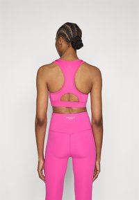 Bustieră sport roz aprins cu design racerback și detaliu tăiat. Asortată cu colanți înalți cu talie înaltă, având un logo.