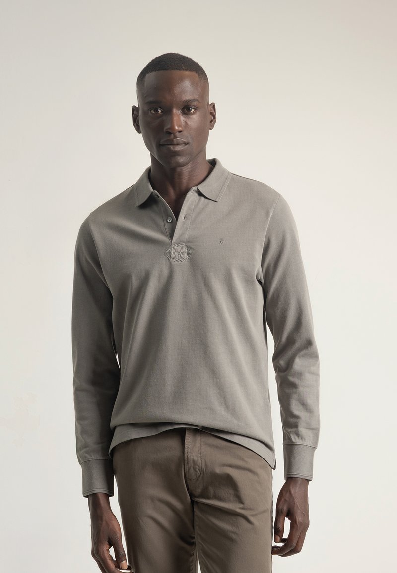 Camisa polo de manga larga en algodón gris claro con cuello, tapeta de tres botones y un sutil detalle texturizado en el pecho.