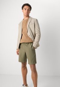 Beige blazer, textured brown sweater, olive green shorts, and white sneakers. The outfit features a mix of tailored and casual elements.