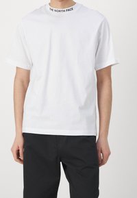 Biała koszulka z krótkim rękawem, z okrągłym dekoltem, z czarnym napisem "THE NORTH FACE". Wykonana z lekkiego materiału o luźnym kroju.