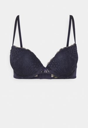Navyblaues Spitzen-BH mit gewellten Kanten, geformten Cups, verstellbaren Trägern und einer Schleifendetail in der Mitte vorne. Strukturiertes Blumendesign.