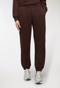 Brązowe dresy z elastycznym pasem i mankietami, charakteryzujące się miękką teksturą oraz bocznymi kieszeniami, w połączeniu z srebrnymi butami sportowymi.