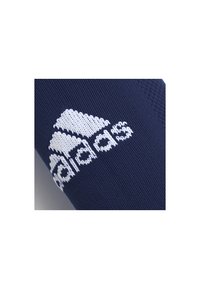 Logotipo blanco de Adidas tejido en tela azul marino, probablemente una prenda de ropa o ropa deportiva.