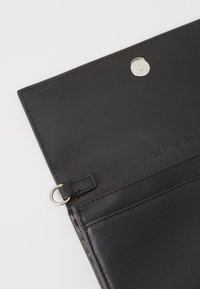 Portafoglio in pelle nera con texture liscia, dotato di chiusura a scatto, slot per carte e nome del marchio in rilievo con lettere discrete.