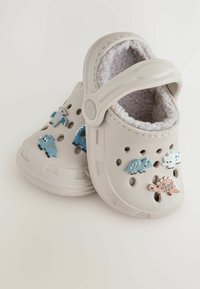 Sabots gris clair avec un intérieur en peluche, ornés d'accents décoratifs de dinosaures en bleu, gris et beige. Conception perforée pour la ventilation.