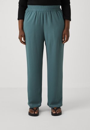 Let hvert, tekstureret, teal bukser med elastisk talje, brede ben og en afslappet pasform, sammen med sorte flip-flops.