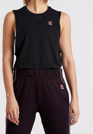 Personne portant un haut noir sans manches et un pantalon noir avec de petits logos carrés multicolores sur la poitrine et la hanche.