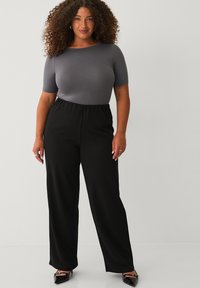 Top gris de manga corta combinado con pantalones negros de corte holgado. La tela parece suave; los pantalones tienen cintura elástica y un diseño de pierna ancha.