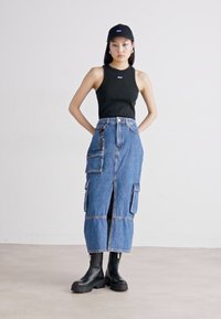Black sleeveless top, knee-length blue denim skirt with cargo pockets, and black chunky-soled boots. Simple black cap with logo.