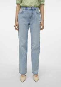 Vaqueros rectos de mezclilla azul claro con cintura alta, que cuentan con bolsillos delanteros y un ligero desgaste, combinados con zapatos beige de punta afilada.