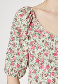 Blusa floral com mangas curtas e bufantes. Apresenta um fundo branco com padrões florais em rosa, vermelho e verde. Tecido texturizado.