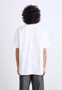 White cotton t-shirt with short sleeves, relaxed fit, and a crew neck. Back view shows simple design with no visible patterns or logos.