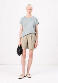 Vaaleansininen raidoitettu lyhythihainen paita yhdistettynä vaaleanruskeisiin shortseihin. Malli pitää mustaa clutch-laukkua, ja hänellä on päällään valkoiset kengät, joissa on hihnatoiminto.