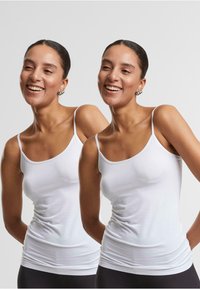 Débardeur en coton blanc avec des bretelles fines, conçu pour être ajusté, texture lisse et léger élasticité. Le haut présente un décolleté arrondi et est semi-ajusté.