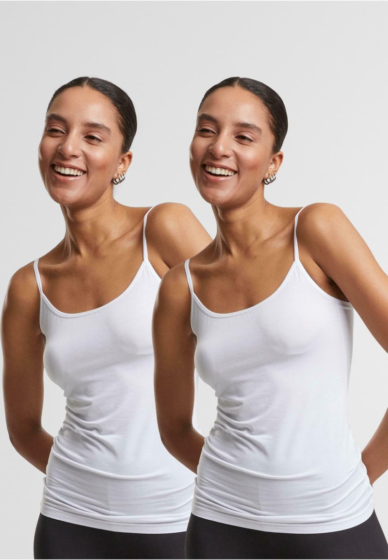 Débardeur en coton blanc avec des bretelles fines, conçu pour être ajusté, texture lisse et léger élasticité. Le haut présente un décolleté arrondi et est semi-ajusté.