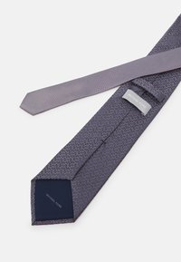 Cravat gri din țesătură texturată, cu un model geometric în gri închis, având un interior solid de culoare bleumarin și o etichetă care spune "MICHAEL KORS."
