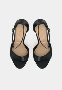 Black strappy sandals with a smooth leather finish, featuring a wide front band and an ankle strap secured with a gold buckle. Beige insole.