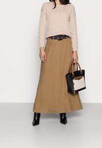 Světlý béžový pletený svetr s texturovaným vzorem, kombinovaný s dlouhou hnědou lněnou sukní. Černé kotníkové kozačky a dvoubarevná kabelka doplňují vzhled.