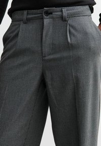 Pantalones a cuadros en blanco y negro con un corte entallado. Cuentan con frente plano, bolsillos laterales y una textura sutil para una apariencia estructurada.